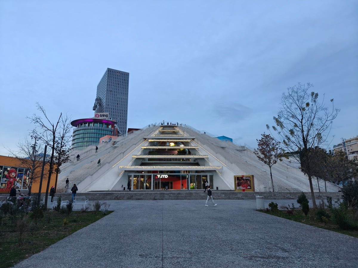 La Pirámide de Tirana, con su fachada triangular escalonada de paneles metálicos, iluminada al atardecer en pleno centro de la ciudad.