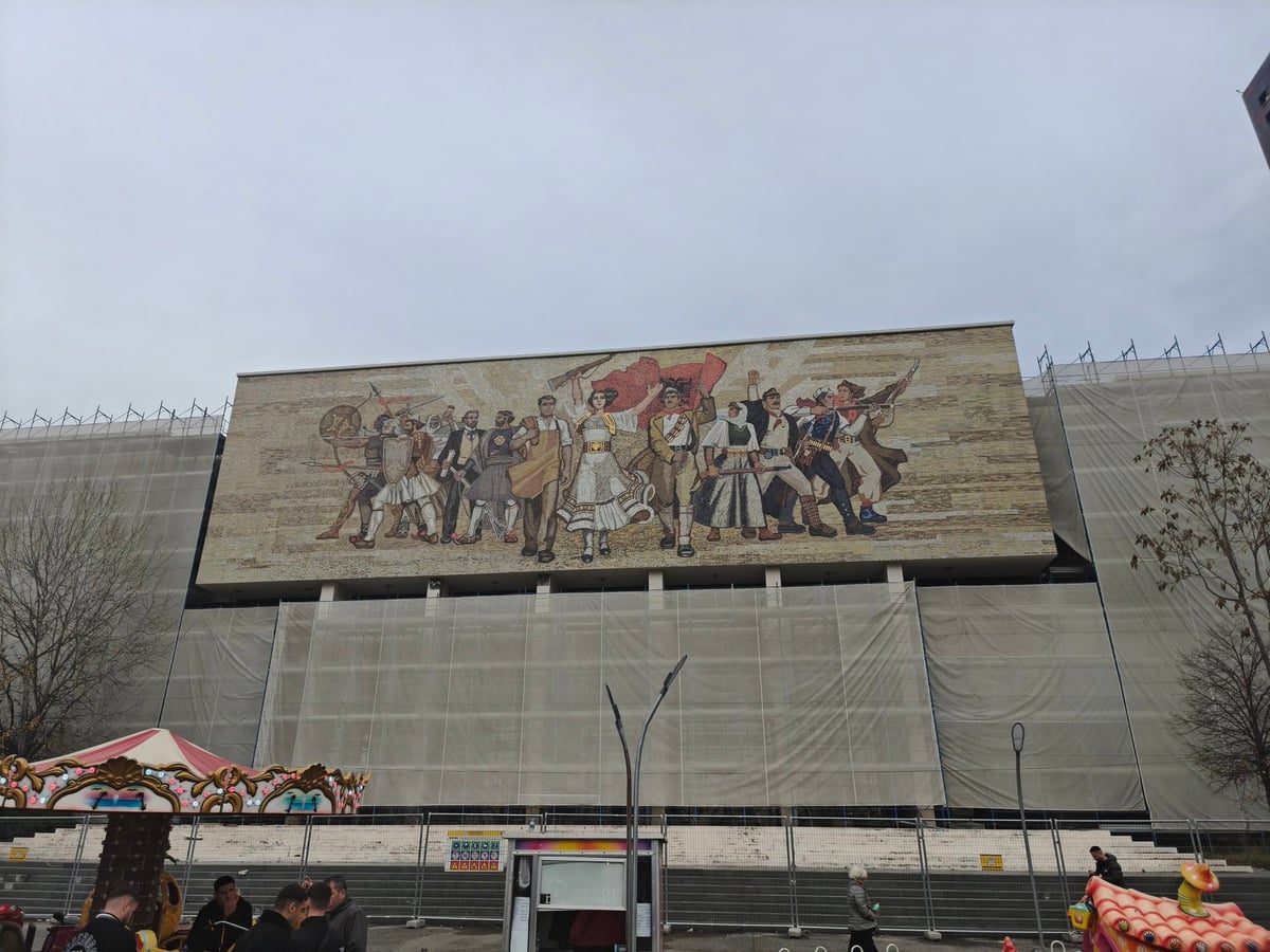 Mosaico monumental con figuras históricas en la fachada de un edificio de Tirana.