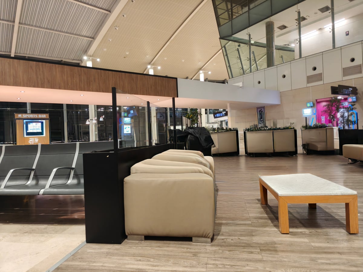 Una sala de espera de aeropuerto con hileras de asientos vacíos y los paneles de información de vuelos al fondo.