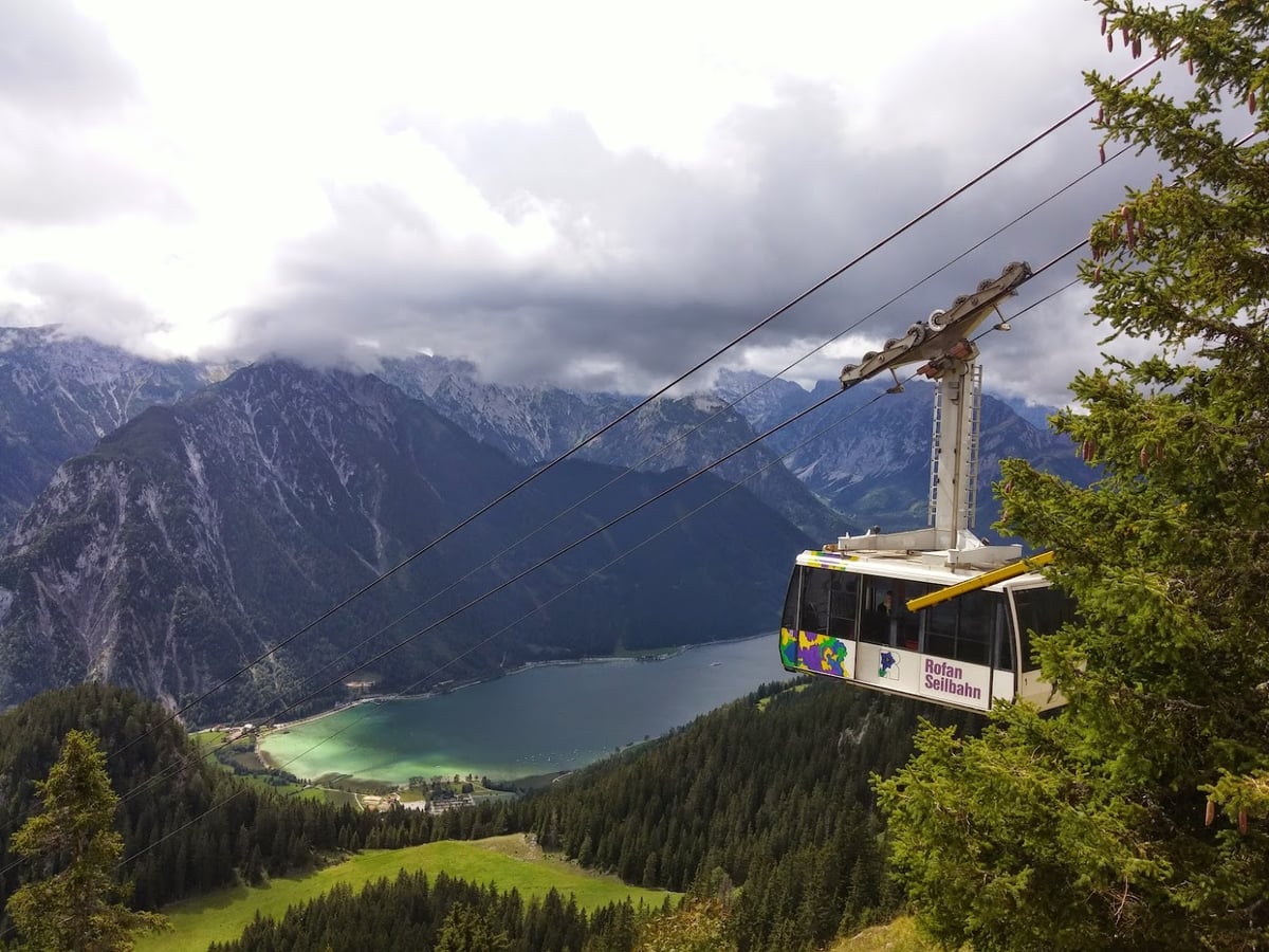 Un teleférico ascendiendo sobre un lago alpino del Tirol austriaco, rodeado de bosques y montañas.