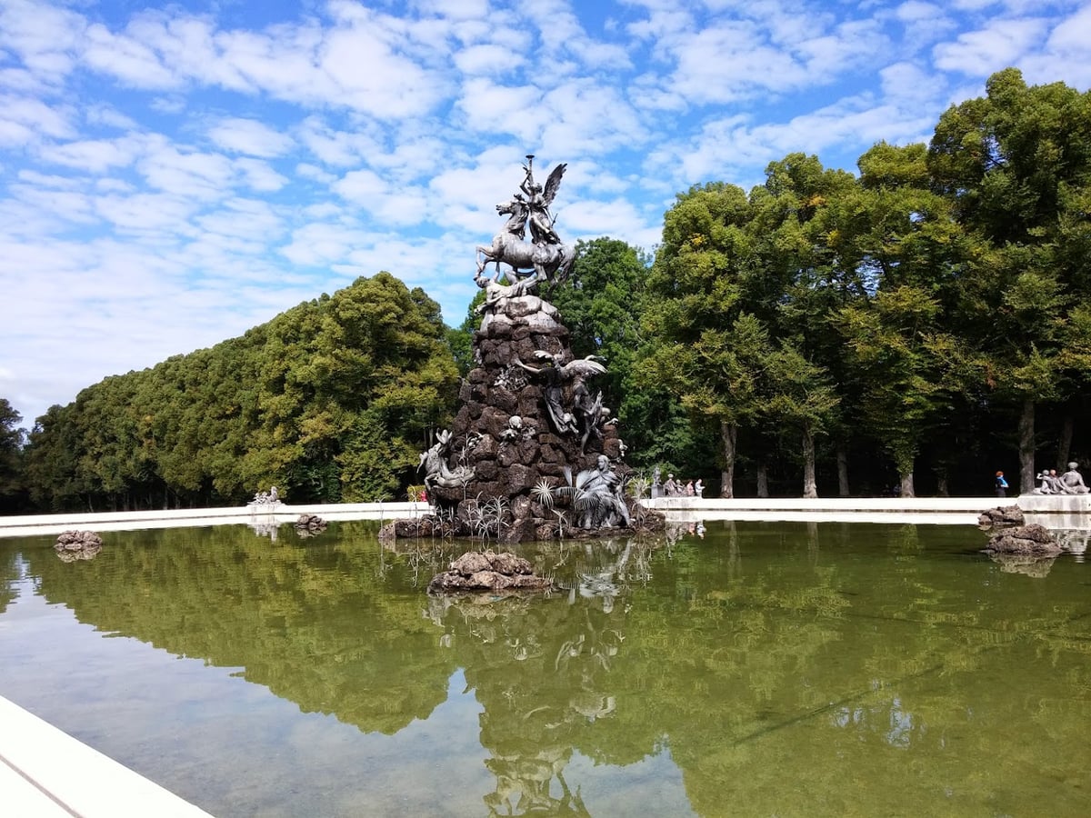 Monumento escultórico junto a un estanque en un parque rodeado de árboles.