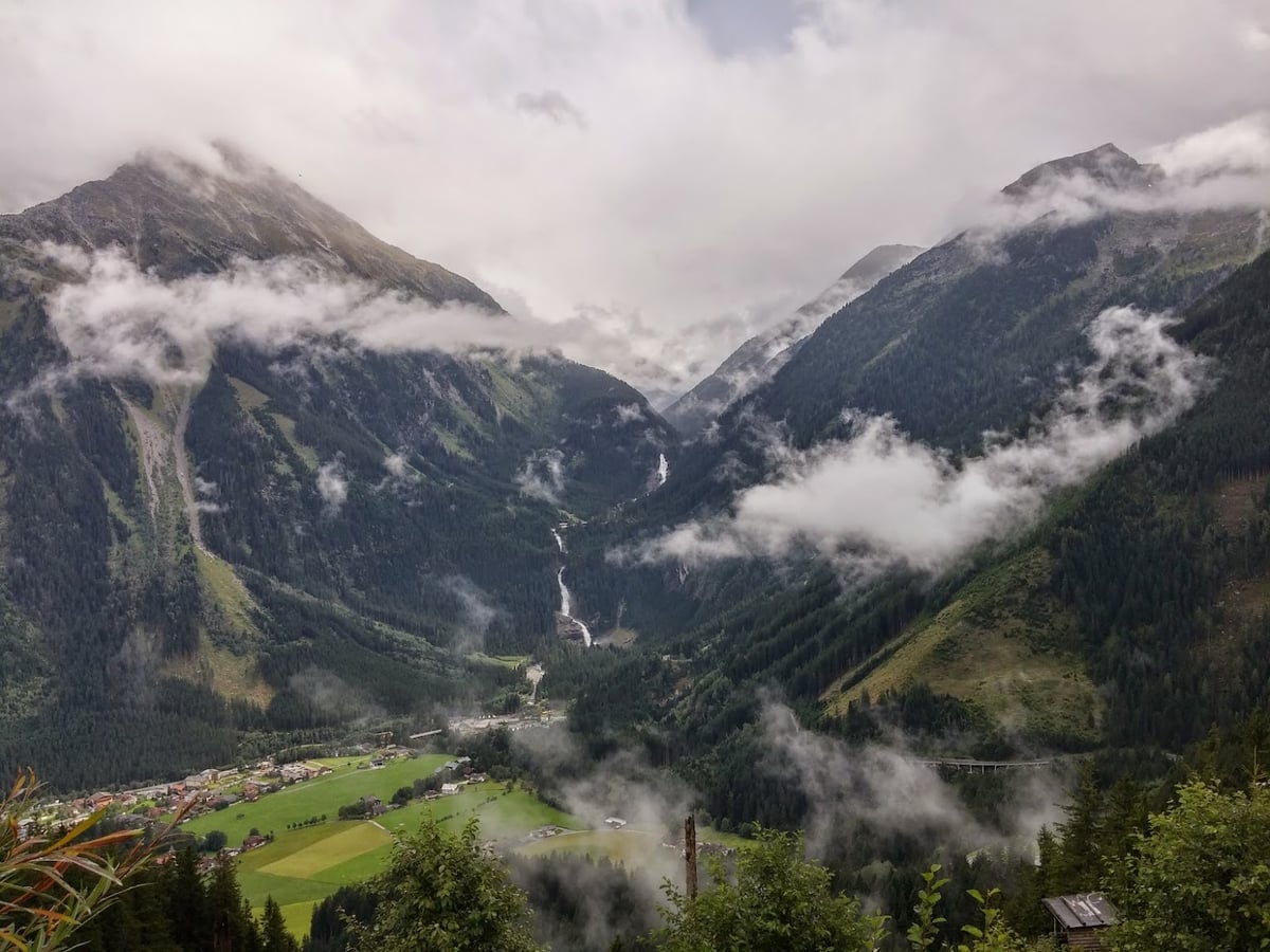 Valle alpino rodeado de montañas y cubierto parcialmente por nubes bajas.