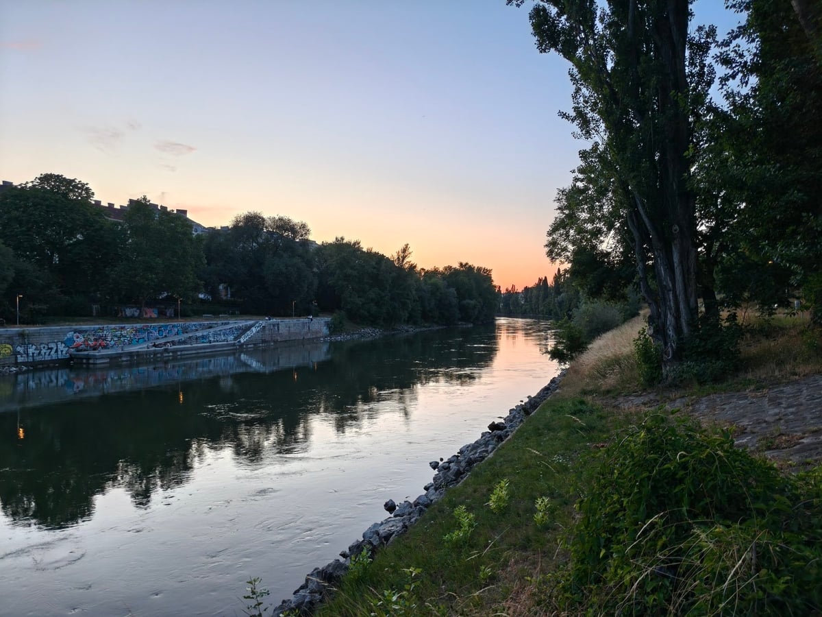 El canal del Danubio en Viena al atardecer, con un muro de grafitis en la orilla y el cielo naranja reflejado en el agua.