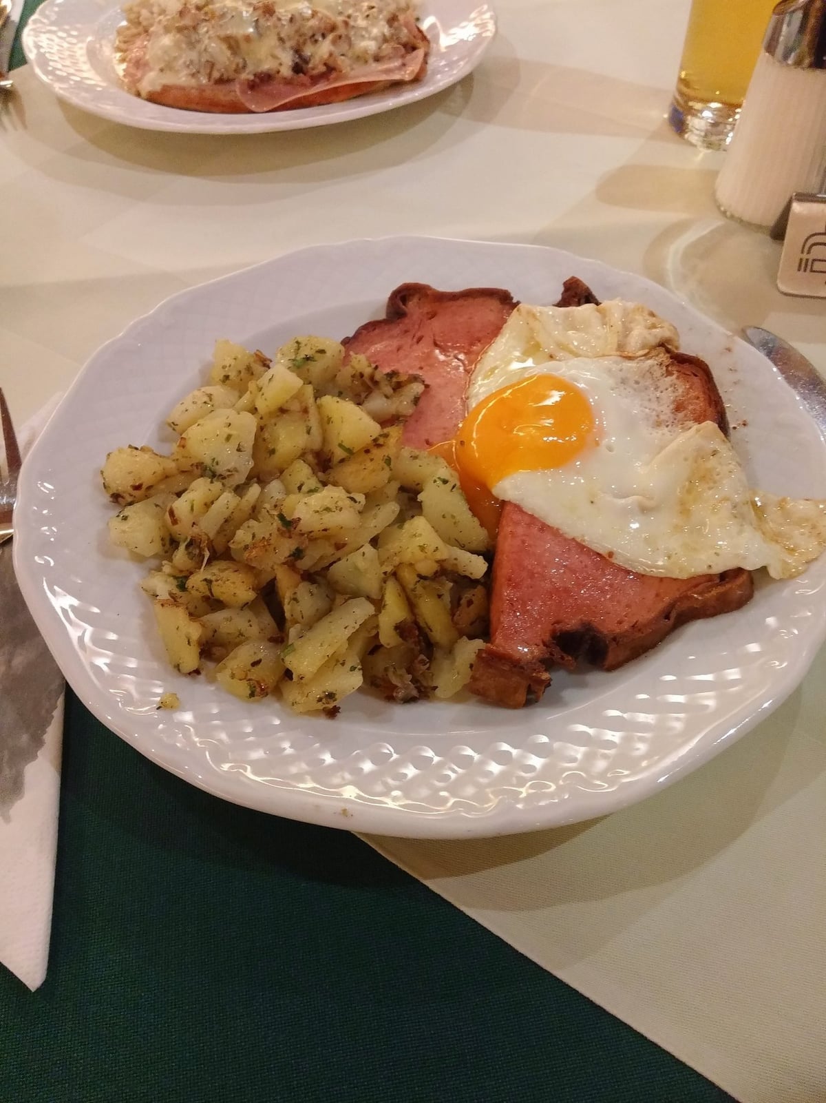 Un plato austriaco con huevo frito, jamón a la plancha y patatas salteadas, con una cerveza al fondo.