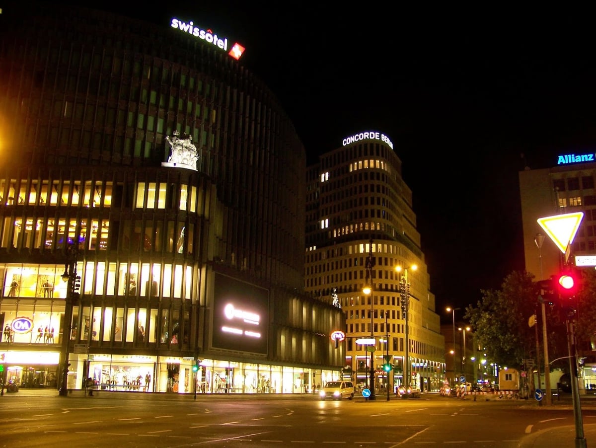 Cruce iluminado de Kurfürstendamm en Berlín con edificios comerciales y hoteles.