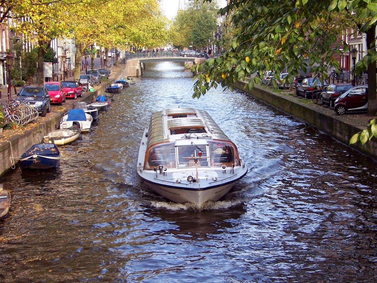 Un canal del barrio de De Wallen en Ámsterdam, con una embarcación turística navegando entre las casas, de día.