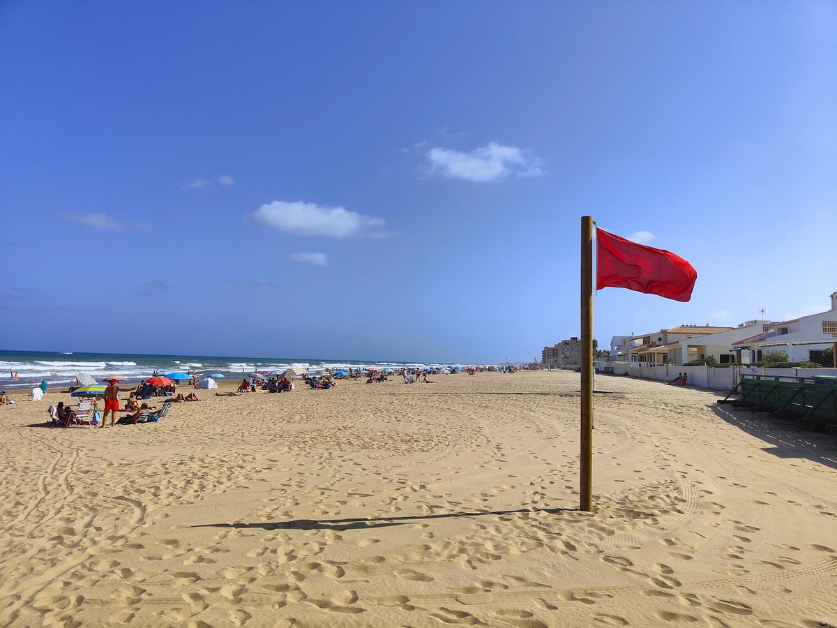 Playa con bandera roja y sombrillas
