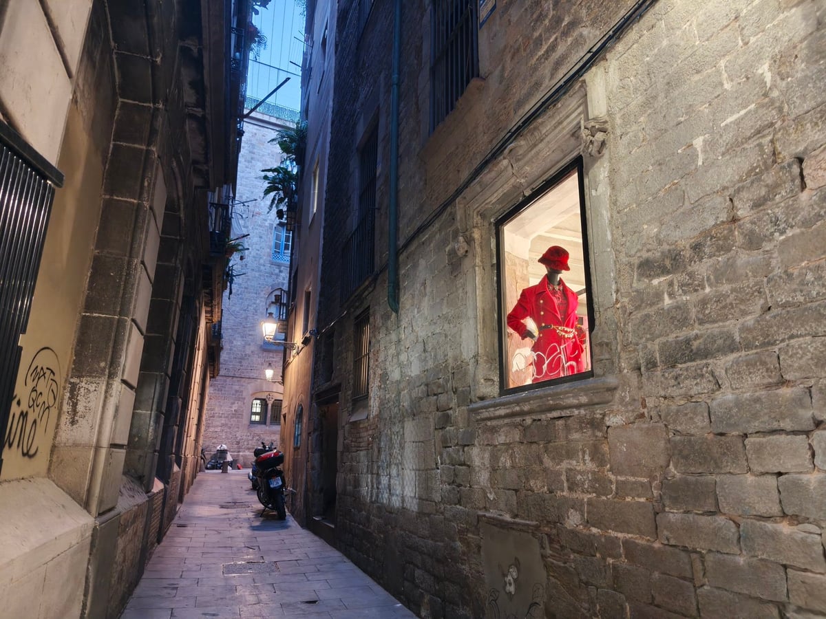 Un callejón del Barri Gòtic iluminado de noche, con un escaparate encendido entre las fachadas de piedra