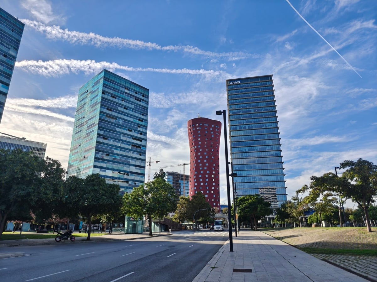 Tres rascacielos de L'Hospitalet de Llobregat junto a la Fira, dos de cristal azulado y una torre cilíndrica roja entre ellos, bajo un cielo con nubes largas y finas.