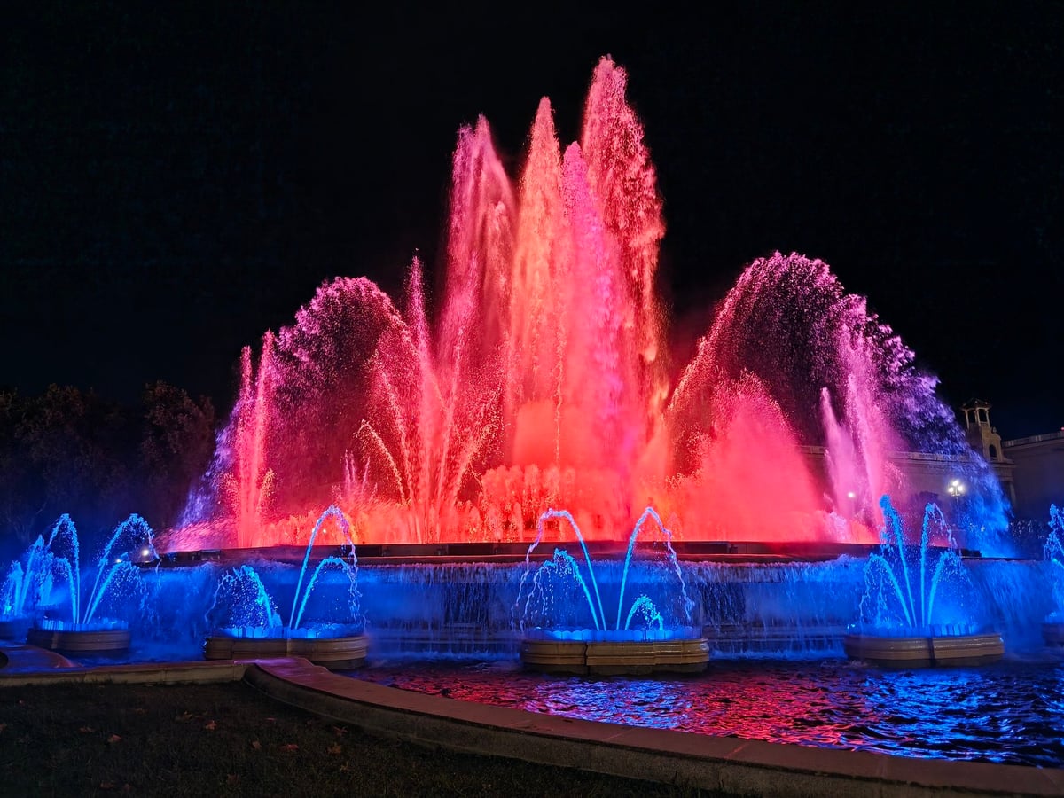 Los chorros de la Font Màgica en rojo, naranja y azul, con el agua formando abanicos en la oscuridad.