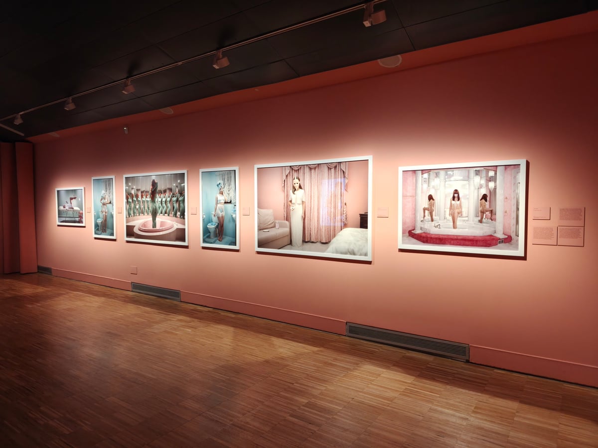 Pared salmón del CCCB con seis fotografías de gran formato en marcos blancos: escenas en tonos pastel de una mujer en baños azules y rosas, en un jacuzzi rodeado de espejos y, con una máscara blanca, en un dormitorio de cortinas rosas.
