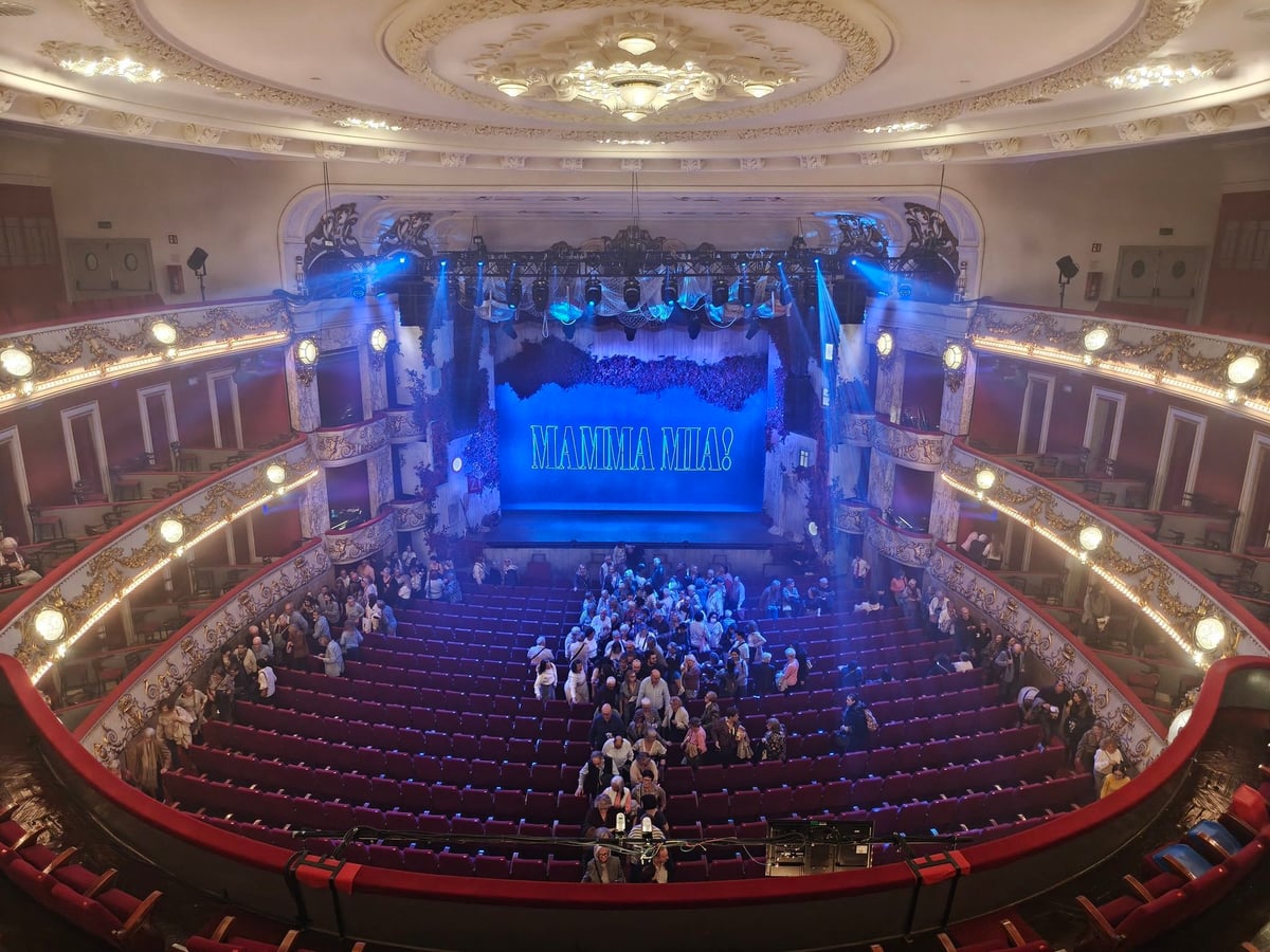 Interior del Teatre Tívoli visto desde la última fila del piso de arriba: la platea llena de butacas rojas, los palcos con luces cálidas y el telón azul de Mamma Mia! al fondo.