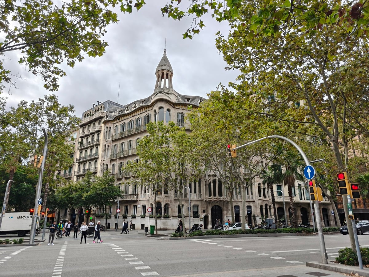 Edificio modernista de Barcelona en una esquina, con un torreón de pizarra, balcones corridos y plátanos frente a la fachada.