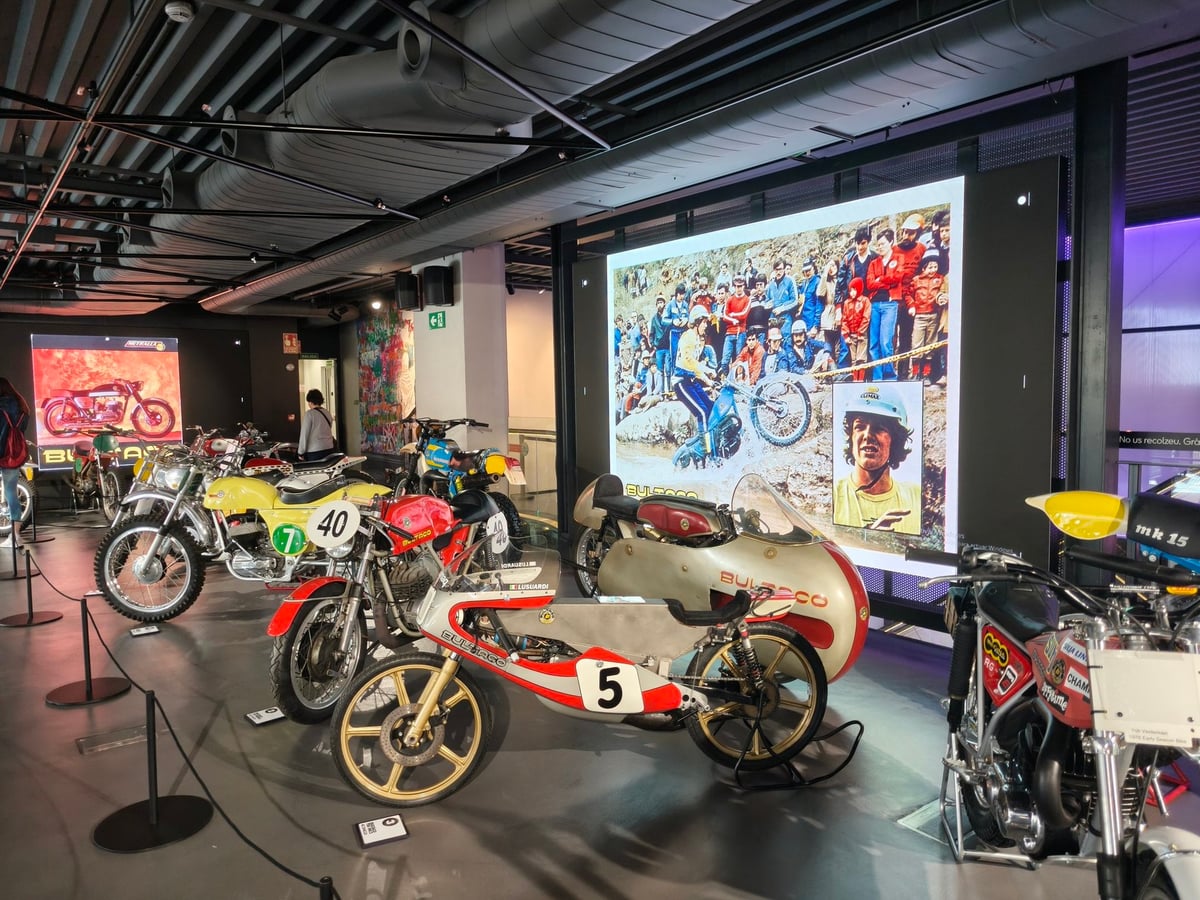 Sala de Casa SEAT con motos clásicas de competición expuestas y una gran pantalla que proyecta una fotografía de carreras.