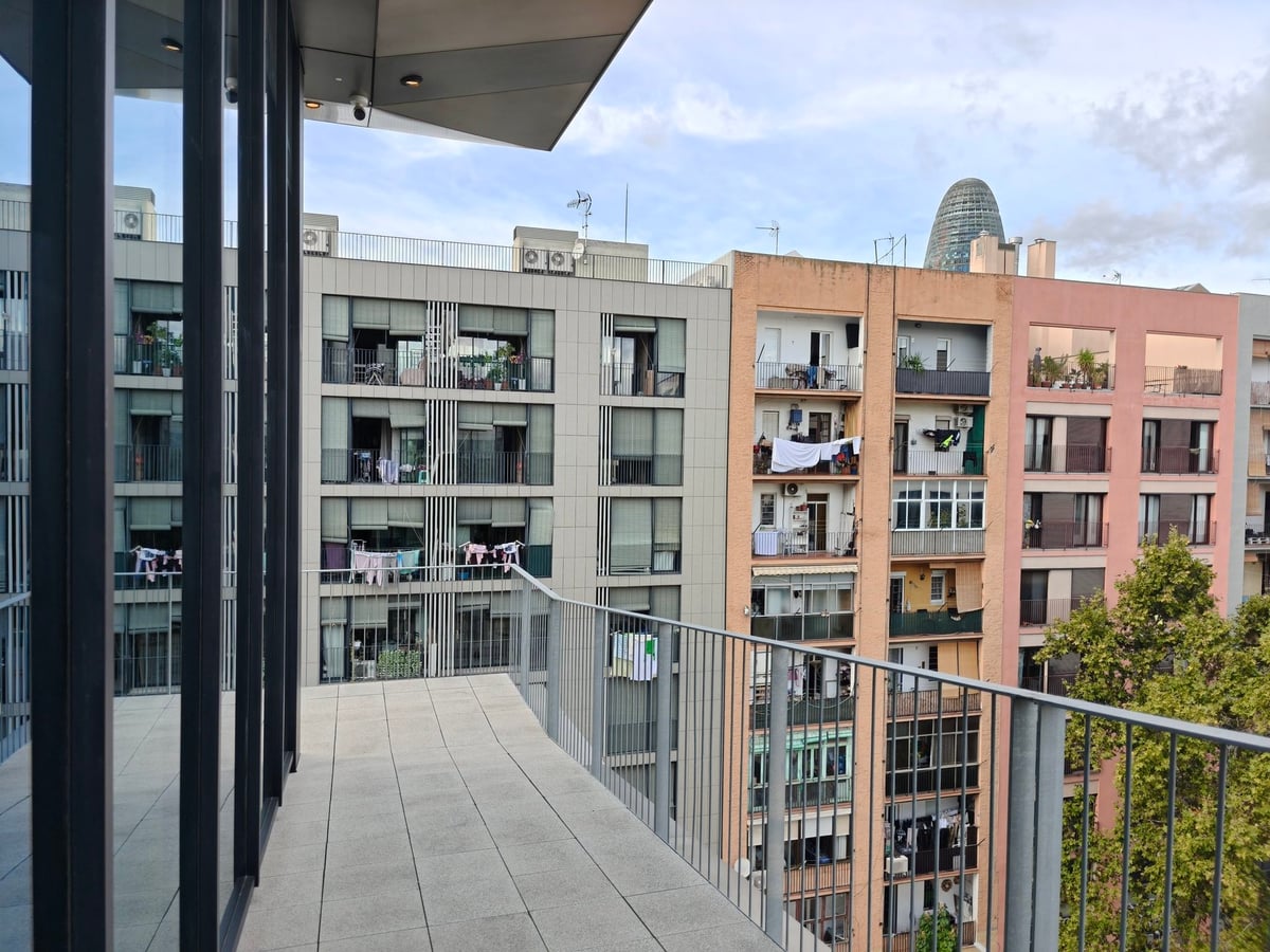 Terraza del campus de LCI Barcelona con barandilla de vidrio y vista a edificios de viviendas y, al fondo, la Torre Glòries.