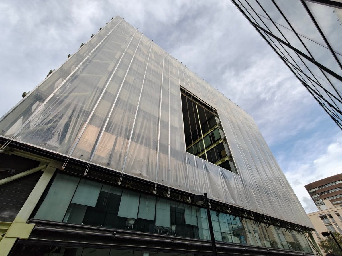 Parte alta del Media-TIC, cubierta por una membrana translúcida con pliegues verticales y una ventana abierta en el volumen, bajo un cielo nublado.