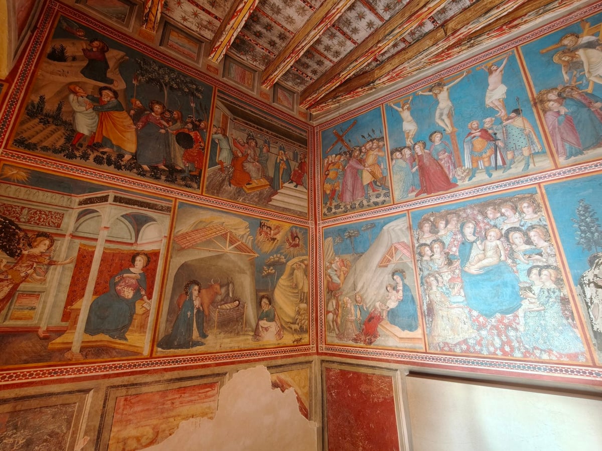 Pinturas murales en rojos y azules con escenas de la vida de Cristo, entre ellas la Natividad y la Crucifixión, en las paredes y el techo de una capilla.