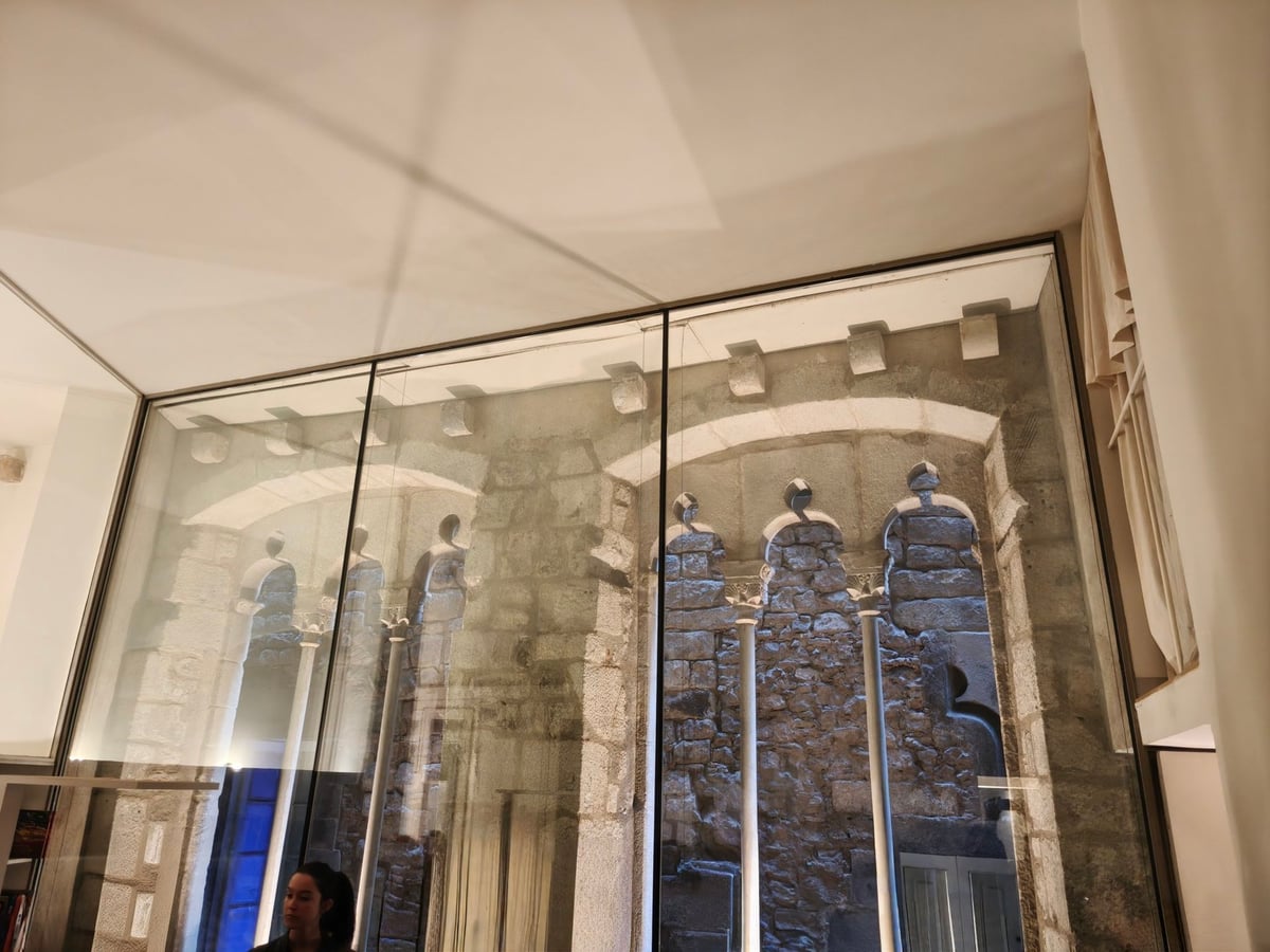 Cristalera que deja ver los restos de una antigua pared de piedra con arcos, en una sala de Casa Adret.
