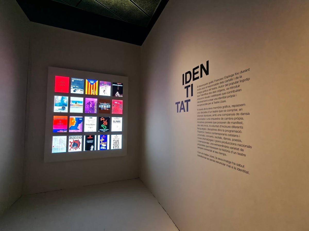 Rincón de la exposición del Teatre Lliure con una cuadrícula iluminada de carteles de obras y la palabra «IDENTITAT» escrita en la pared.