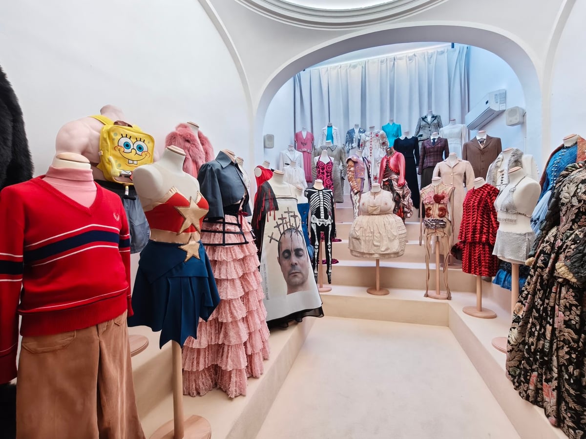 Maniquíes con vestuario de teatro en una sala con arco: un jersey rojo, vestidos con volantes rosas, un disfraz con una estrella y un bolso de Bob Esponja.