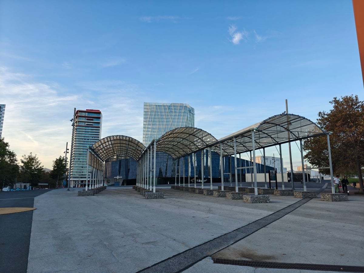 Marquesinas metálicas curvas de una plaza de Diagonal Mar, con torres de oficinas detrás, al caer la tarde.