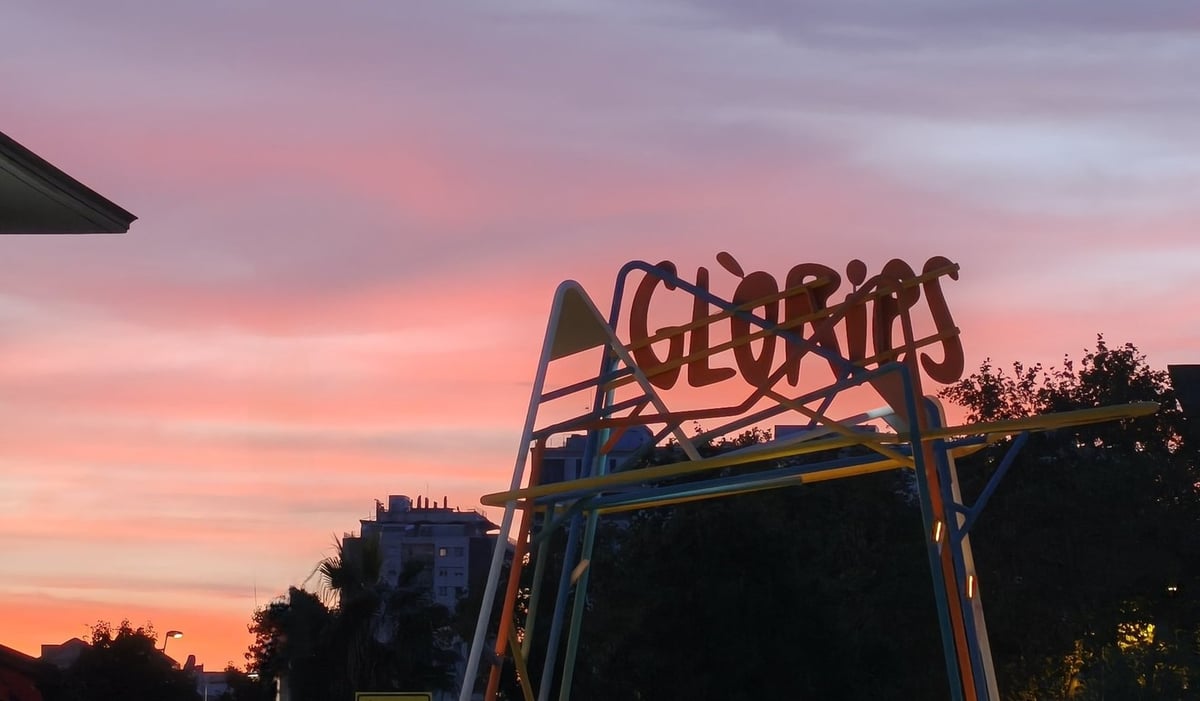 El rótulo naranja de GLÒRIES sobre una estructura metálica, contra un cielo rosado al atardecer.