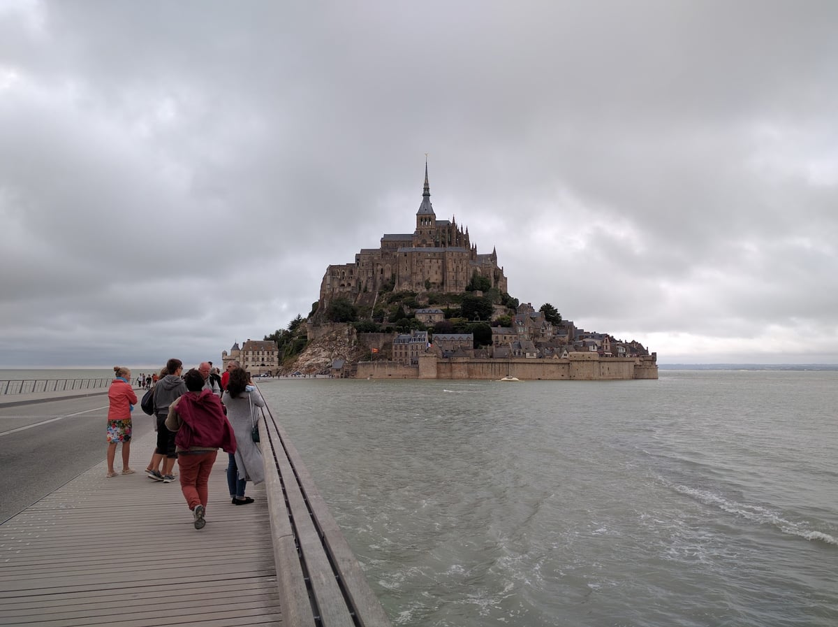 El Mont-Saint-Michel aproximándose desde el puente de acceso, con la abadía sobre la roca y las murallas cayendo hacia la bahía.