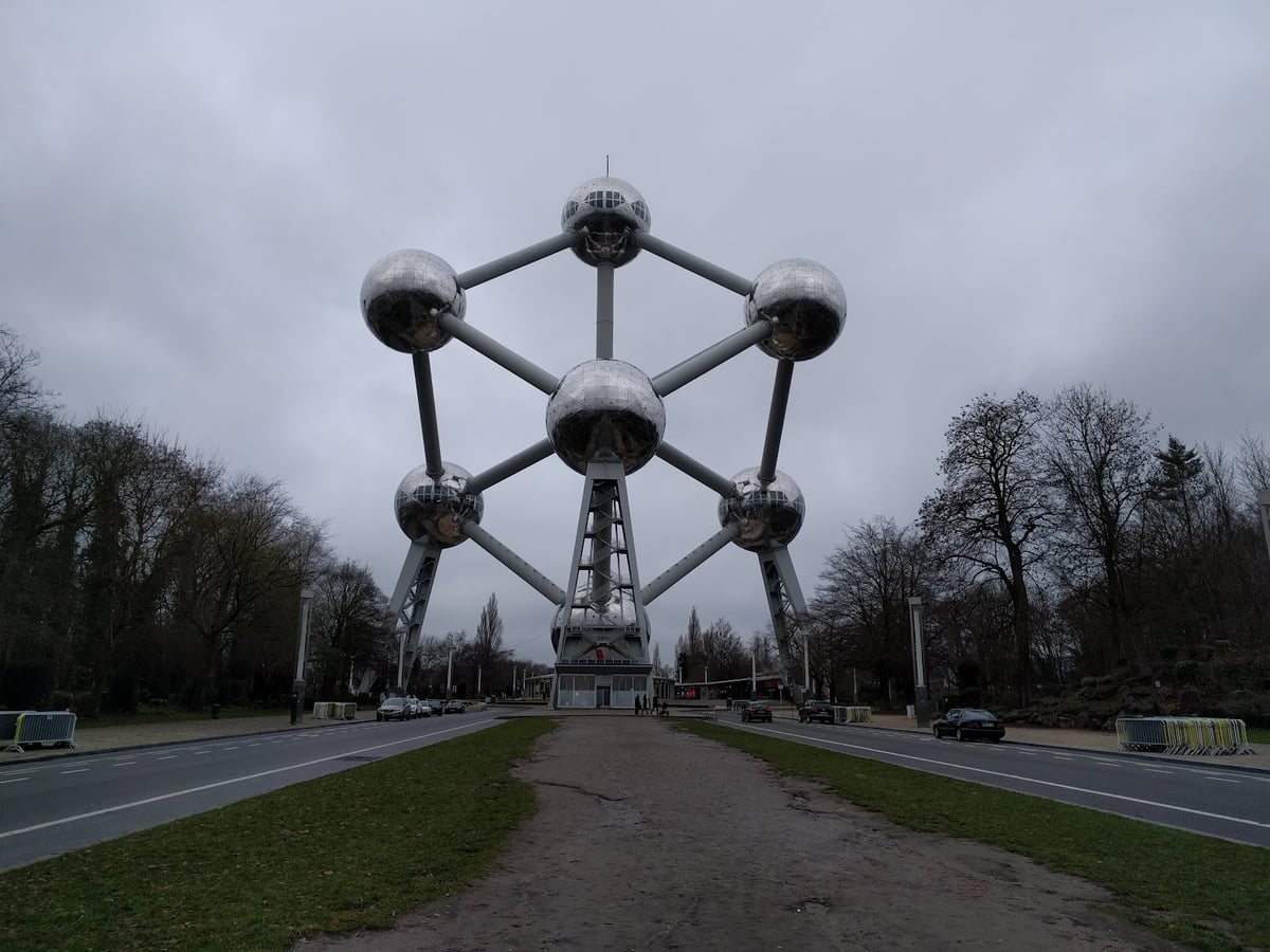 El Atomium de Bruselas en un día gris, con sus nueve esferas de acero pulido unidas por tubos, visto de frente desde la avenida que lleva hasta su base entre árboles pelados de invierno.