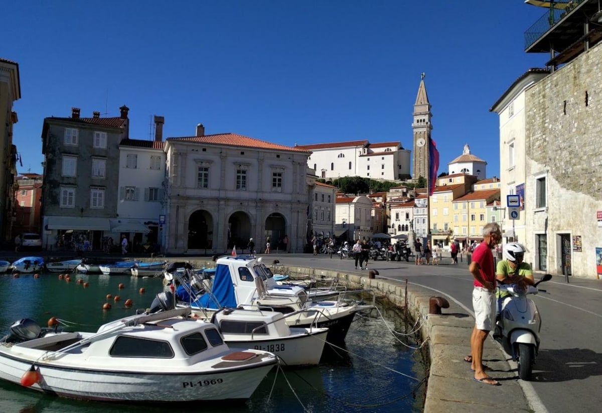 La plaza Tartini de Piran, con el pavimento claro, el ayuntamiento porticado y la estatua del violinista en el centro, y el pequeño puerto interior al fondo.