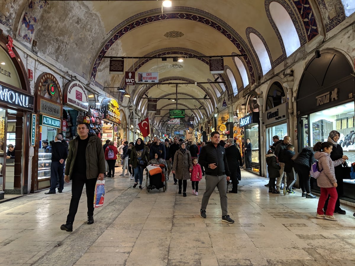 Interior del Gran Bazar de Estambul, con las bóvedas pintadas, las lámparas colgantes y los puestos de alfombras y cerámica a ambos lados de la calle cubierta.