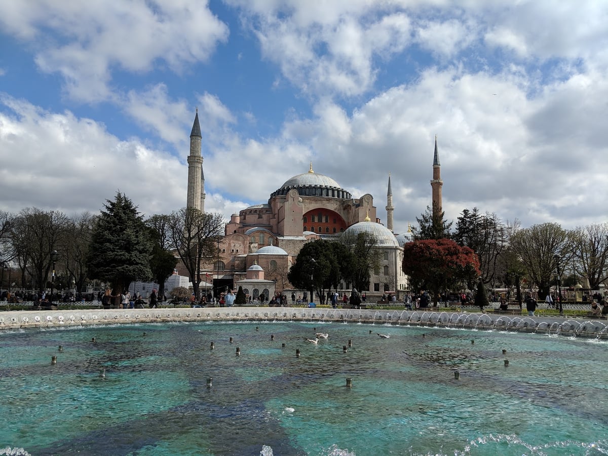 Santa Sofía vista desde los jardines de Sultanahmet, con su gran cúpula, los muros rosados y los cuatro minaretes, y la fuente de la plaza en primer plano lanzando chorros sobre el agua turquesa.