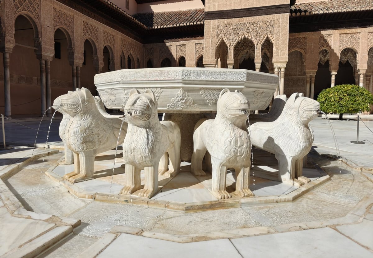 La fuente de los Leones de la Alhambra, con la taza de mármol sostenida por doce leones que echan agua por la boca, en el centro del patio rodeado de arquerías caladas y columnas finas.