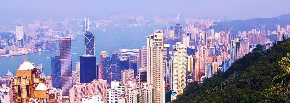 El skyline de Hong Kong visto desde lo alto del Pico Victoria, con las torres del distrito central asomando sobre la ladera boscosa, el puerto al fondo y la península de Kowloon al otro lado del agua.