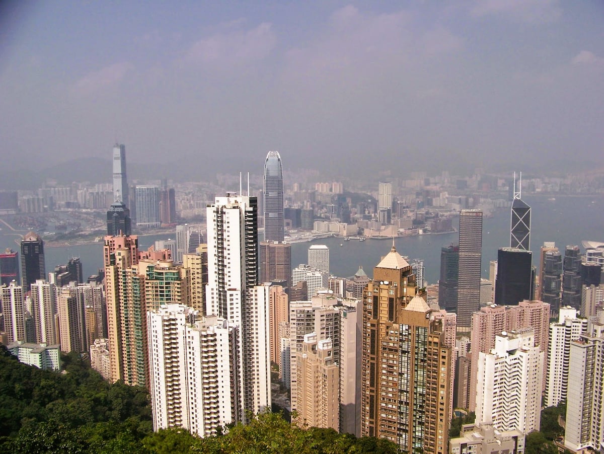 Hong Kong desde el Pico Victoria, con los rascacielos de viviendas apiñados en la ladera boscosa, las torres del distrito central detrás, el puerto cruzándolo todo y Kowloon difuminado en la calima.