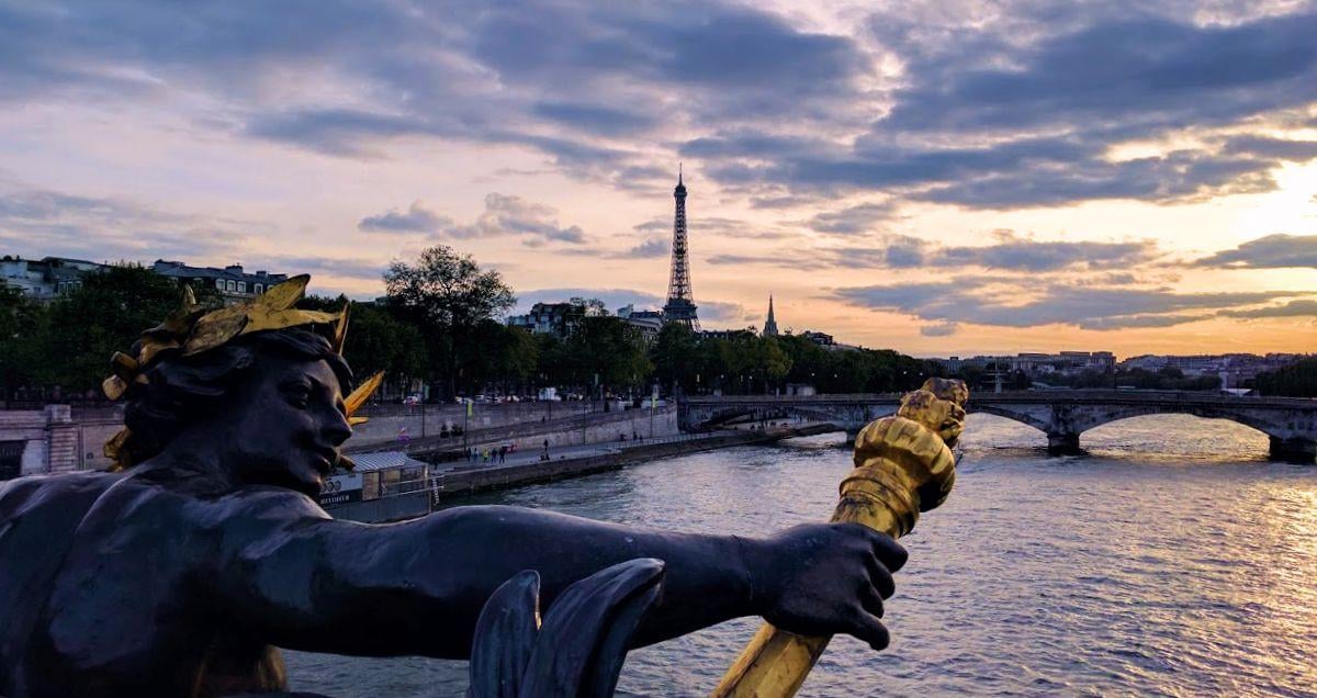 Foto de una estatua en un puente de París, con la torre Eiffel al fondo