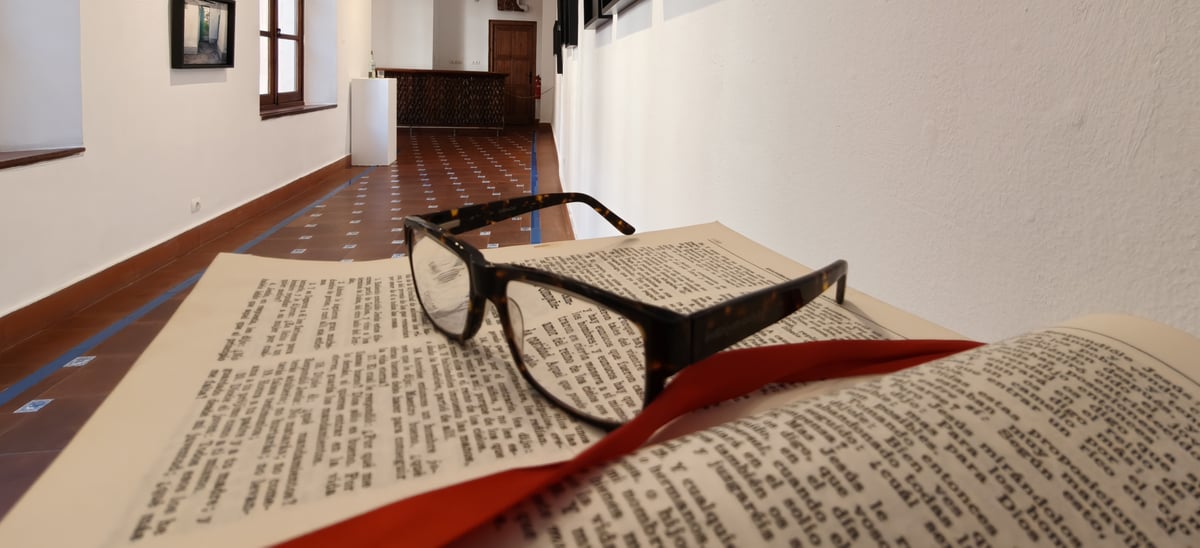 Fotografía de unas gafas sobre un libro abierto en el centro de una habitación alargada