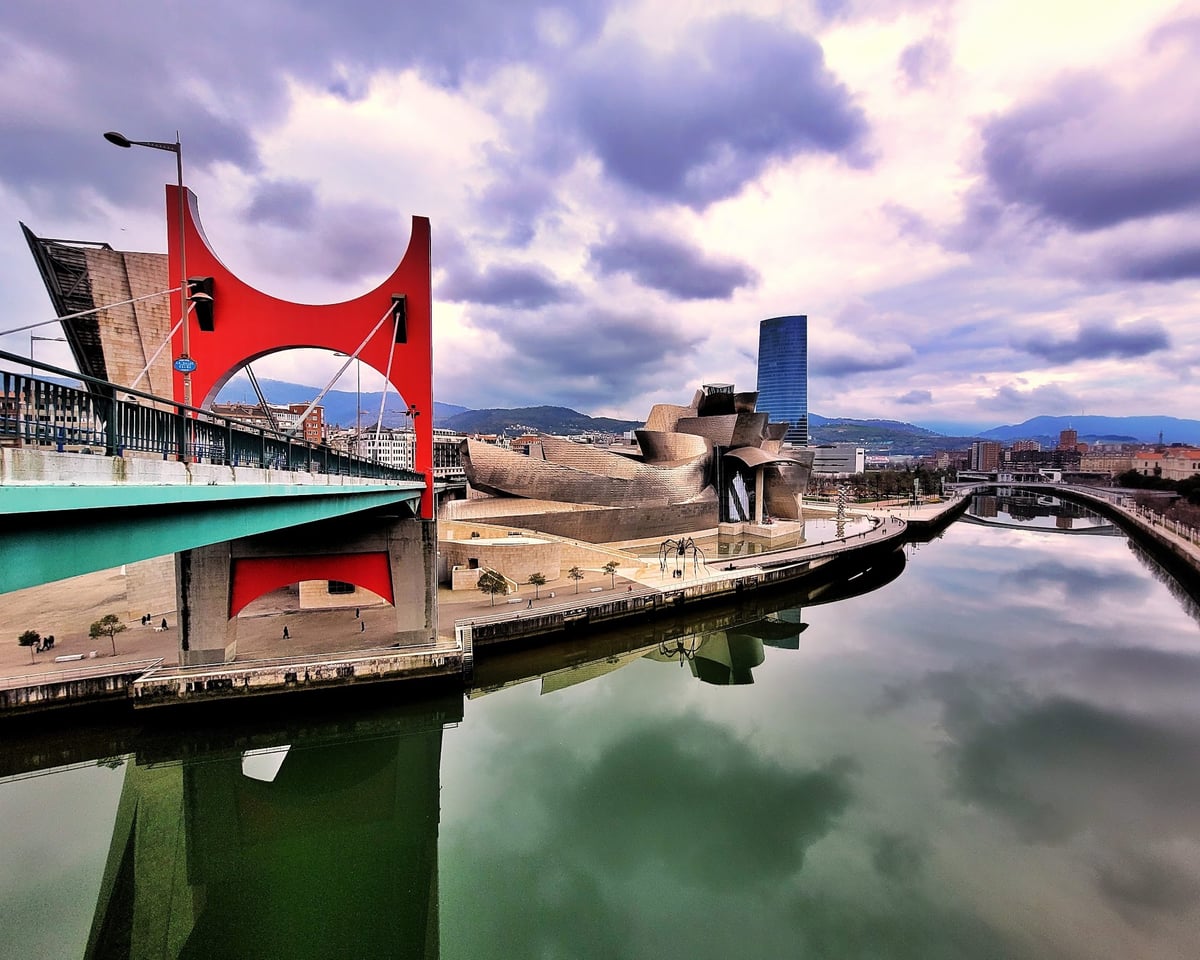 El icónico Museo Guggenheim Bilbao y el puente de La Salve con su distintivo arco rojo, reflejados de cabeza en la ría de Bilbao