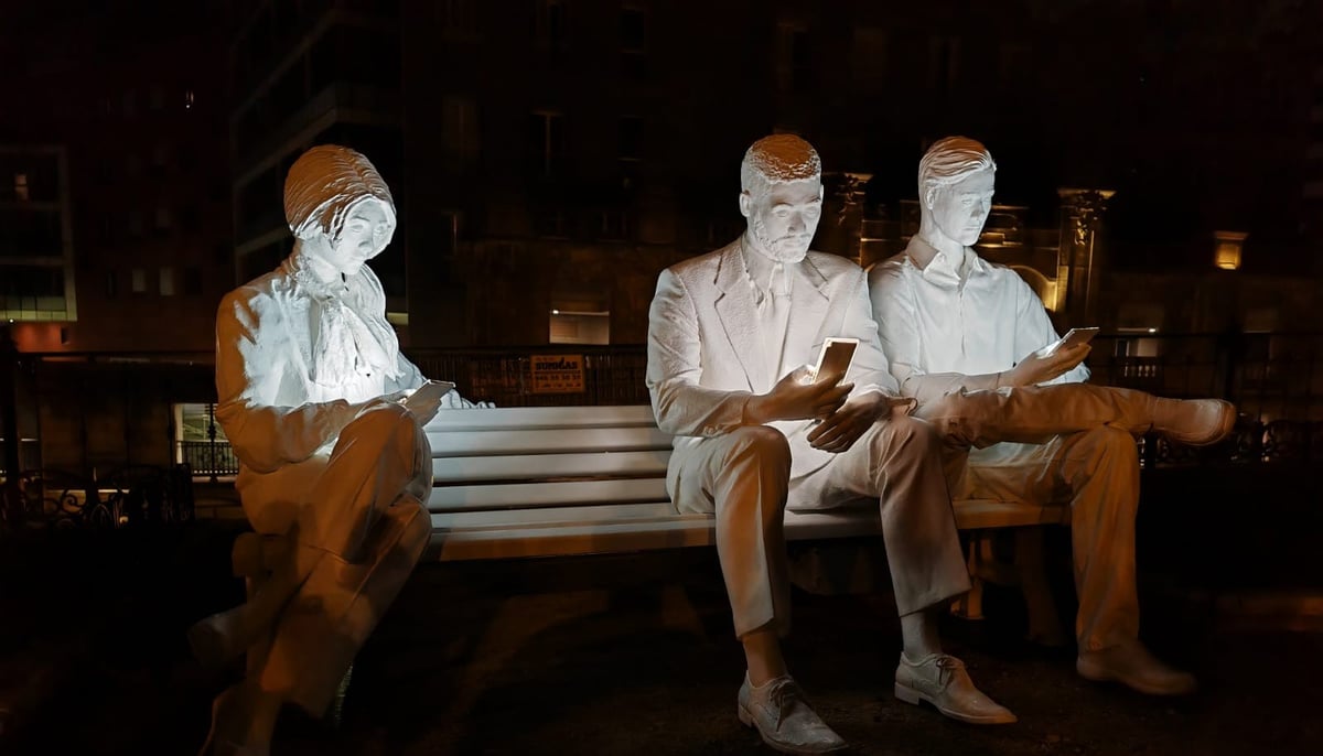 Foto de tres figuras humanas mirando sus teléfonos móviles ajenos a su entorno