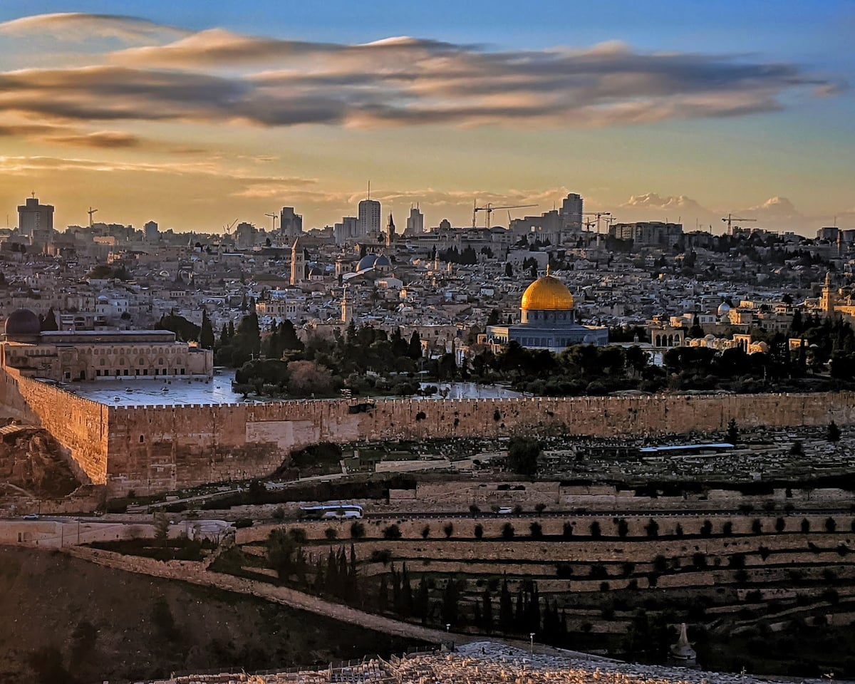 Jerusalén al atardecer desde el monte de los Olivos, con la Cúpula de la Roca dorada en el centro de la explanada, la muralla de piedra recorriendo la ladera y la ciudad vieja extendiéndose detrás.