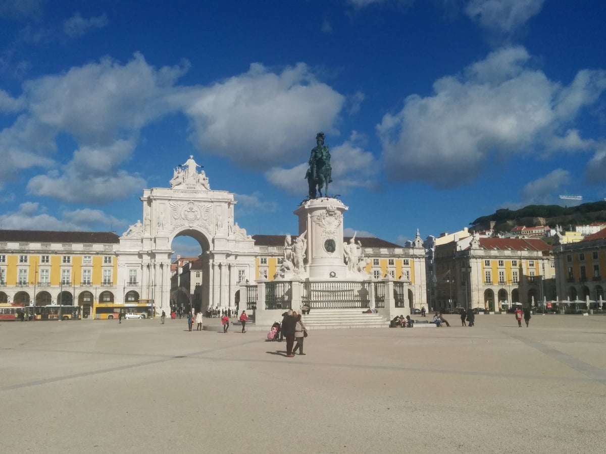 La Praça do Comércio de Lisboa abierta al Tajo, con las arcadas amarillas en tres lados y la estatua ecuestre de José I en el centro.