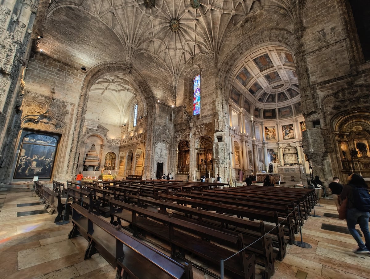 Entrada del Monasterio de los Jerónimos en Belém, con su fachada manuelina labrada y una fila de visitantes esperando junto al muro.