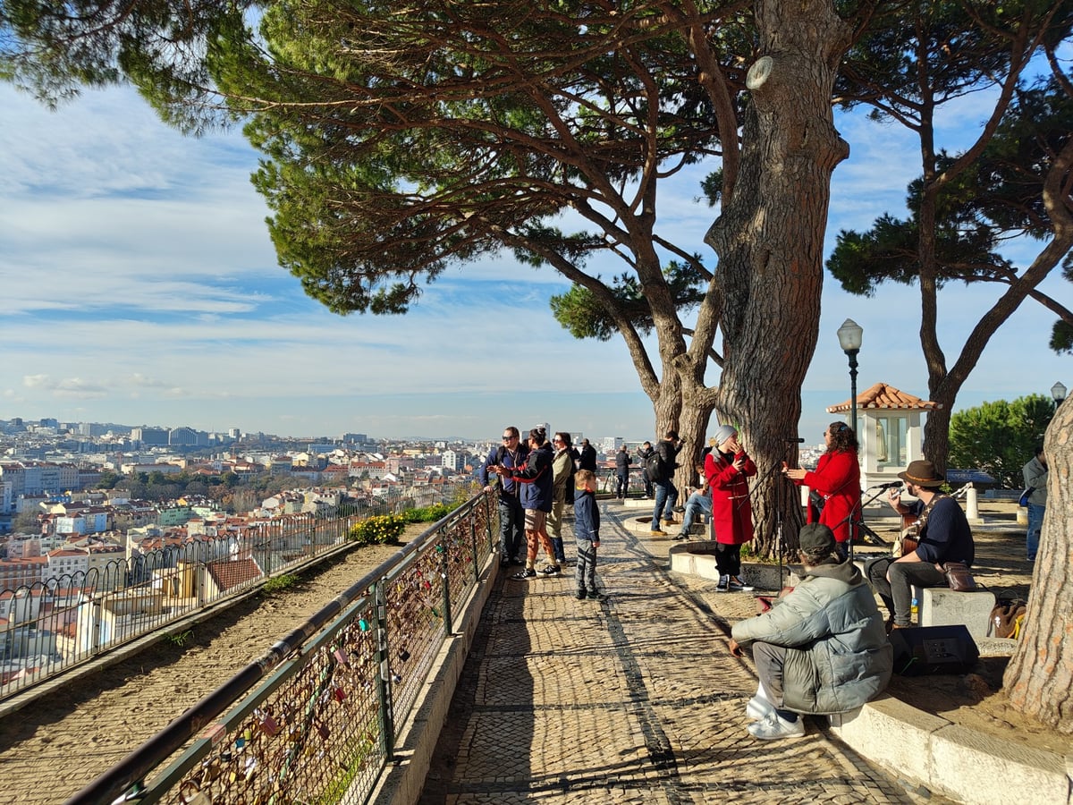 Panorámica de Lisboa desde uno de los miradores altos, con los tejados bajando hacia el Tajo, el castillo en su colina y el puente 25 de Abril al fondo.