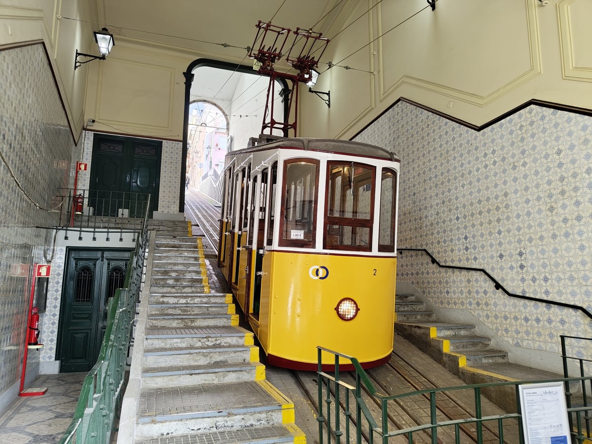 El Elevador da Bica ascendiendo por una calle empinada de Lisboa entre casas de fachadas claras, con la ropa tendida en los balcones y el vagón amarillo en el centro de la imagen.