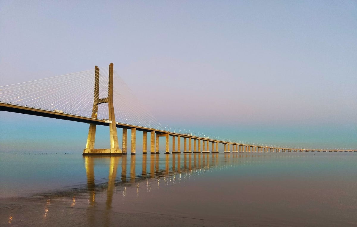 El puente Vasco da Gama al amanecer sobre el Tajo, con su pilono atirantado y la sucesión de vanos perdiéndose en la bruma del estuario.