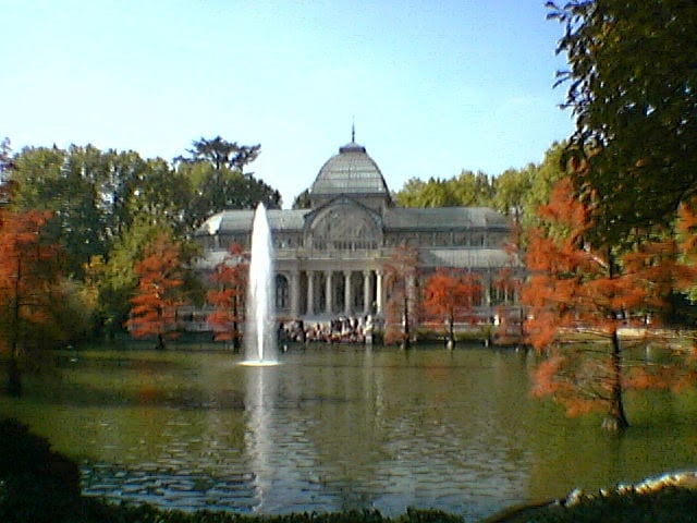 El Palacio de Cristal del Retiro visto desde el estanque, con su estructura de hierro y vidrio reflejada en el agua.