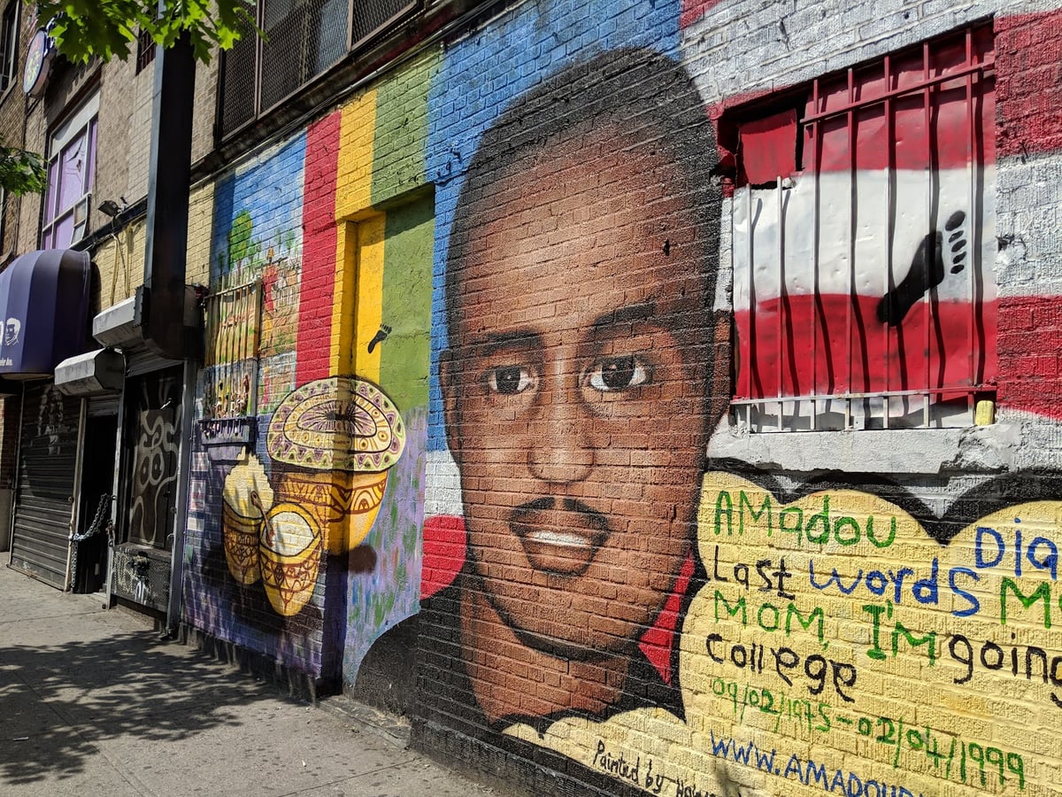 Mural dedicado a Amadou Diallo: su rostro pintado a gran tamaño sobre el ladrillo, con unos djembés y franjas de colores a la izquierda y, a la derecha, un corazón amarillo con sus últimas palabras, «Mom, I'm going to college», y las fechas 09/02/1975 - 02/04/1999.