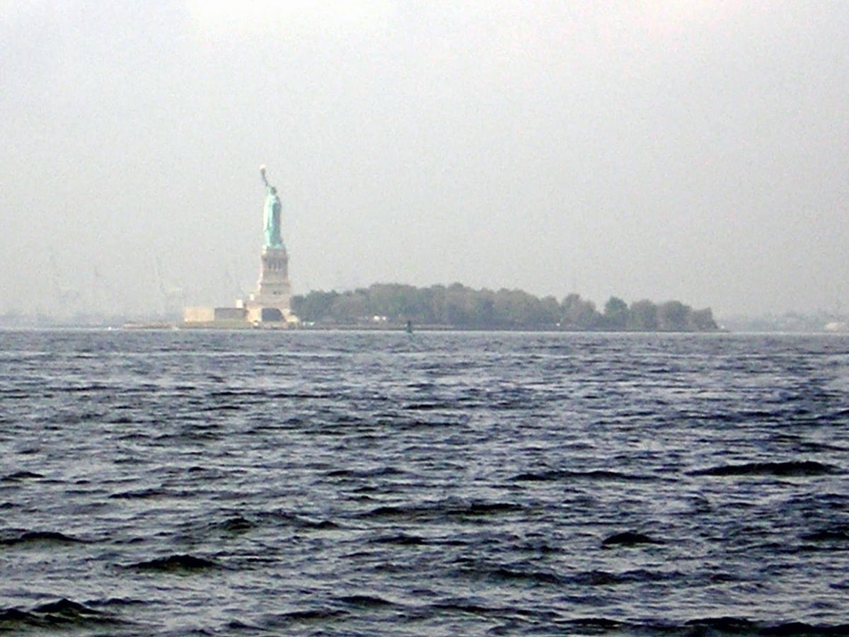 La Estatua de la Libertad recortada en el horizonte del puerto, vista desde la orilla de Battery Park.