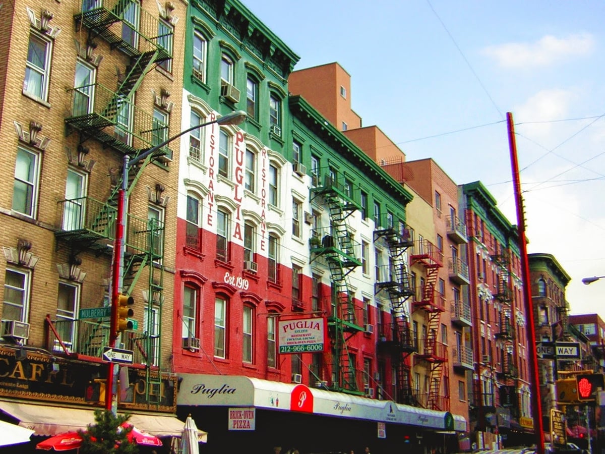 Una calle de Little Italy en Mulberry Street, con manteles de cuadros en las mesas de las terrazas y camareros invitando a entrar desde la puerta.