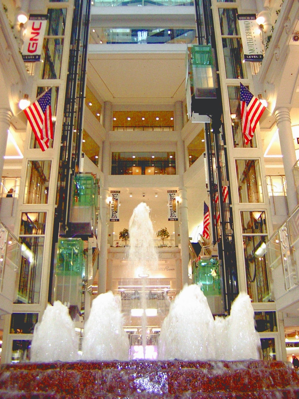 El interior del Manhattan Mall en Herald Square, con varias plantas de tiendas y una cafetería junto a los ventanales.