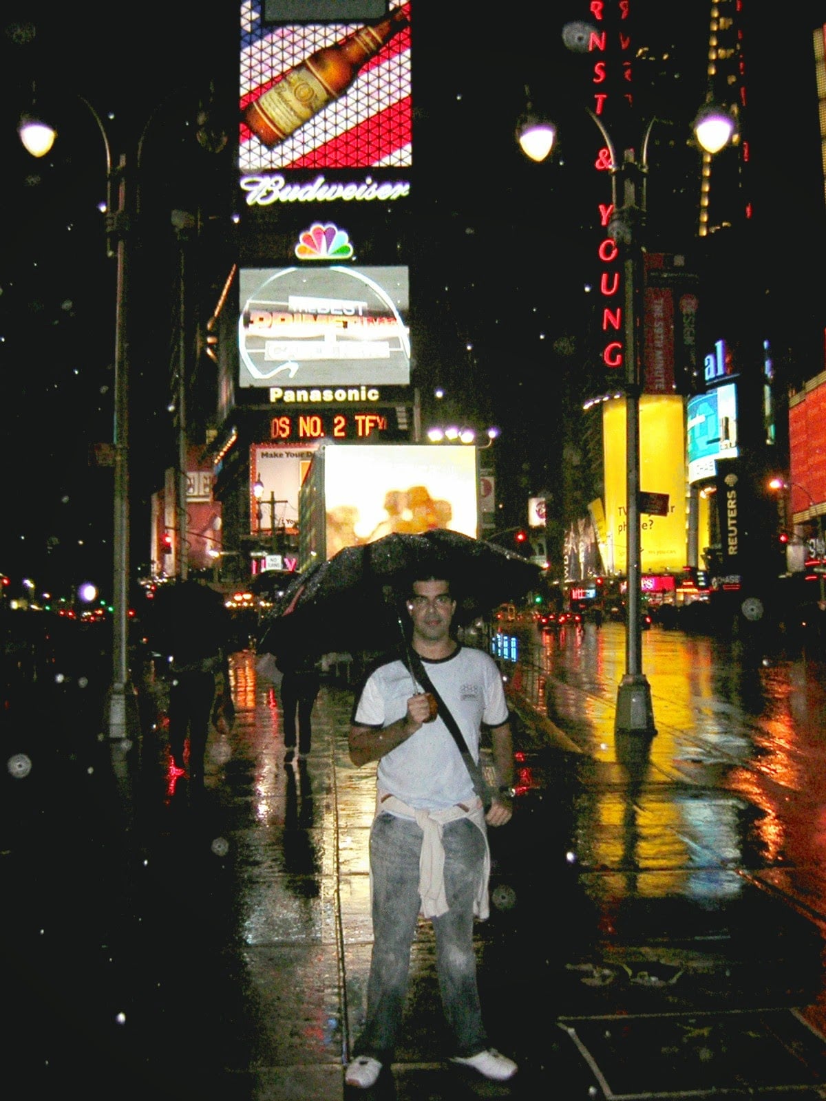 Una calle de Manhattan de noche bajo la lluvia, con los paraguas y las luces de los carteles reflejadas en el asfalto mojado.